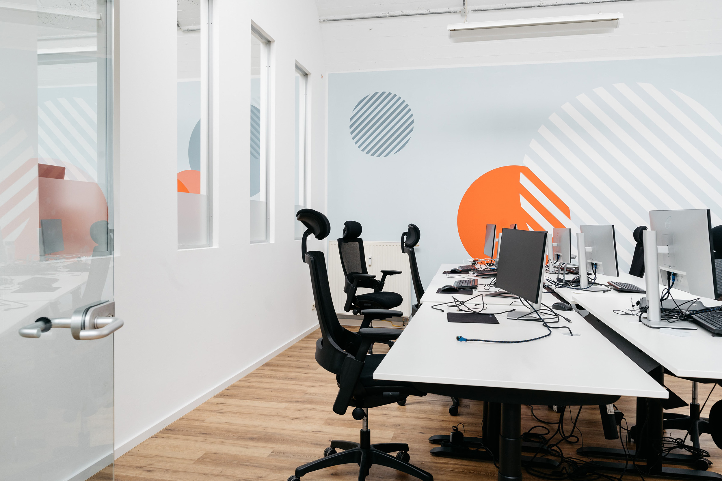 Helle, modern eingerichtete Arbeitsplätze im pace-IT Büro Köln mit ergonomischen Stühlen und farblich gestalteter Wand